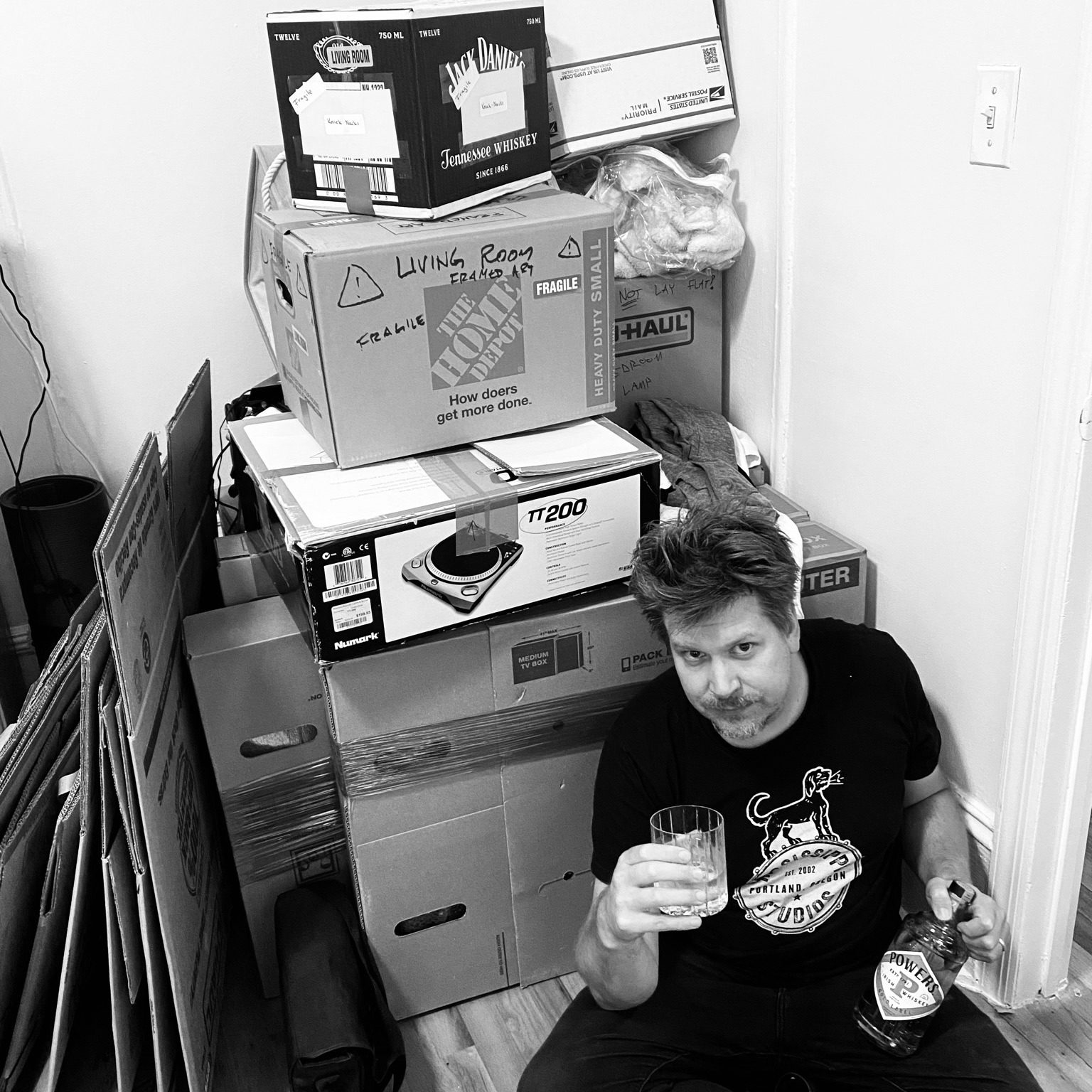 Josh posing with a bottle of whiskey and stacks of moving boxes.