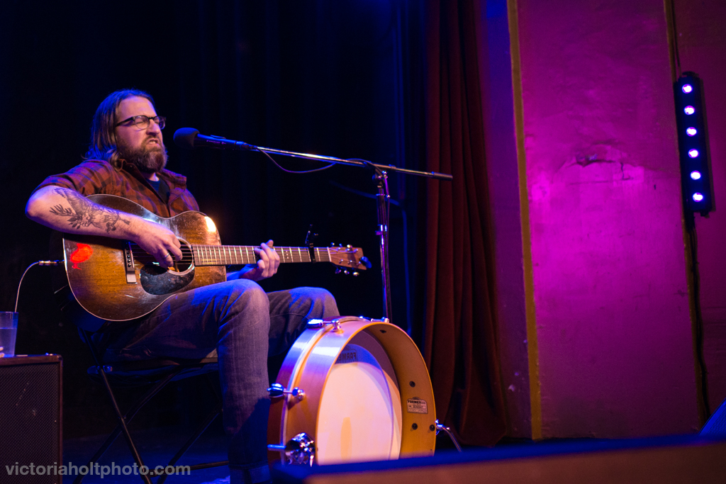 Local Seattle musician Aaron Semer performing with an acoustic guitar in fuchsia lighting. Photo by Victoria Holt.