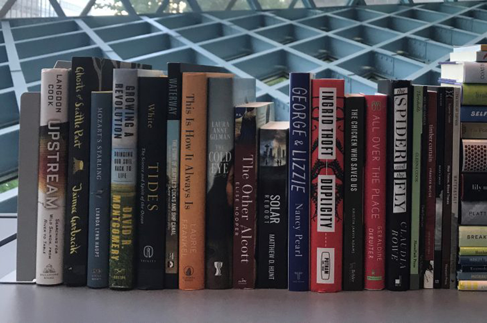 A stack of books that were finalists for the 2018 Washington State Book Award, including Ghosts, on display under the iconic Seattle Public Library curtain wall windows. 