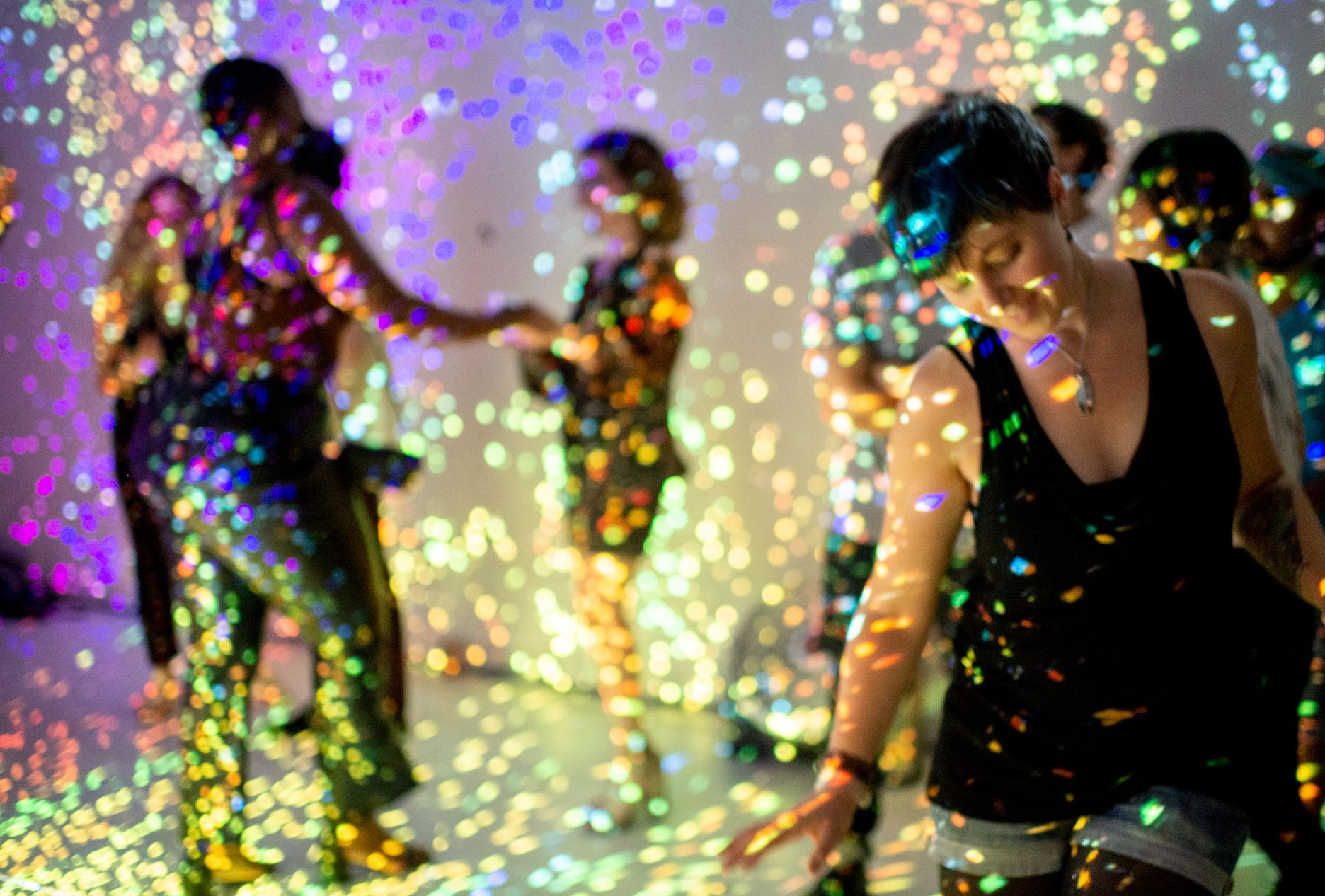 Jaimee and others smiling and dancing under prismatic lighting. Photo by Victoria Holt.